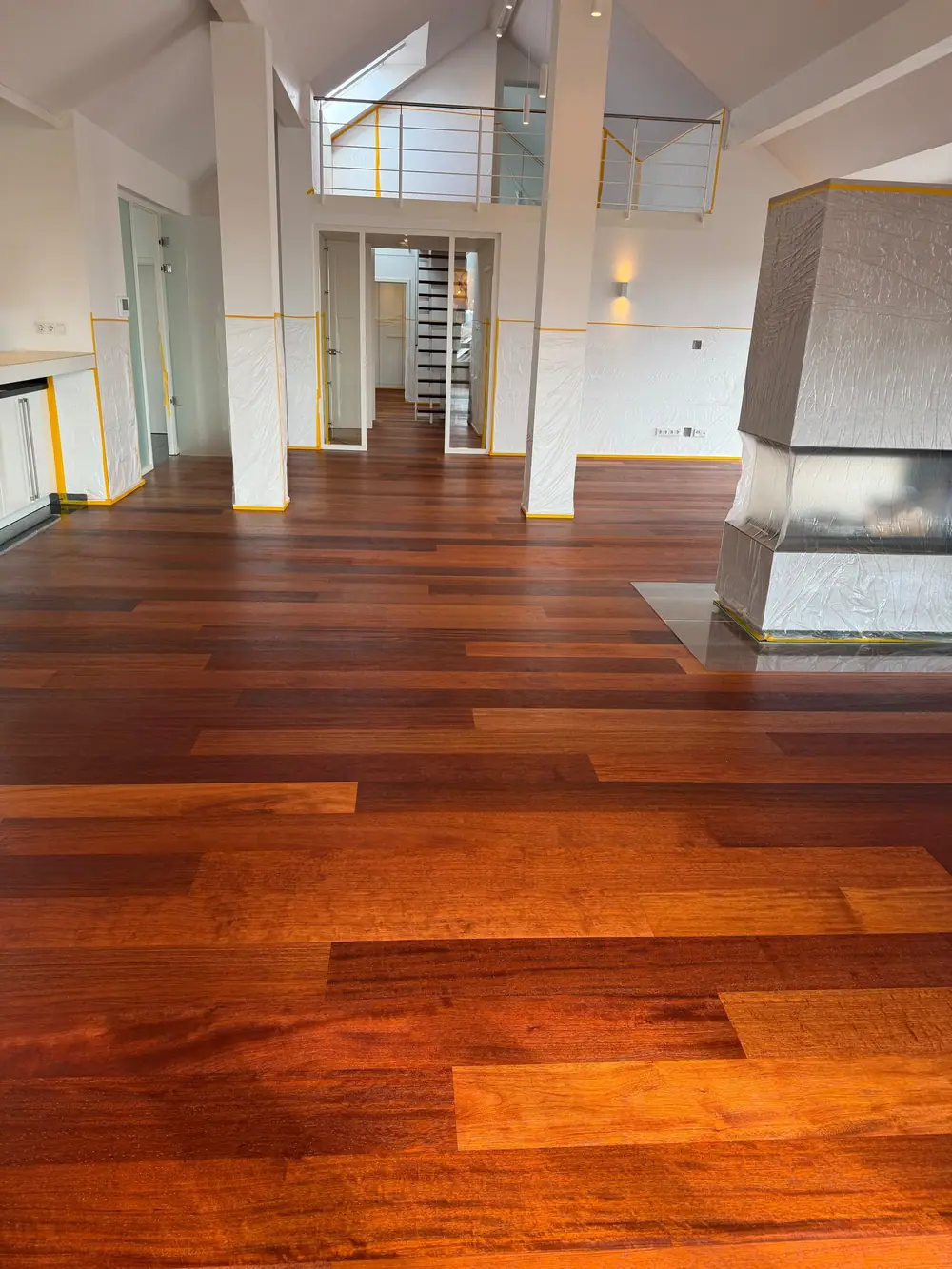 Offener Wohnraum mit dunklem Dielenboden, abgedecktem Kamin, weißen Stützen und Galerie im Hintergrund.