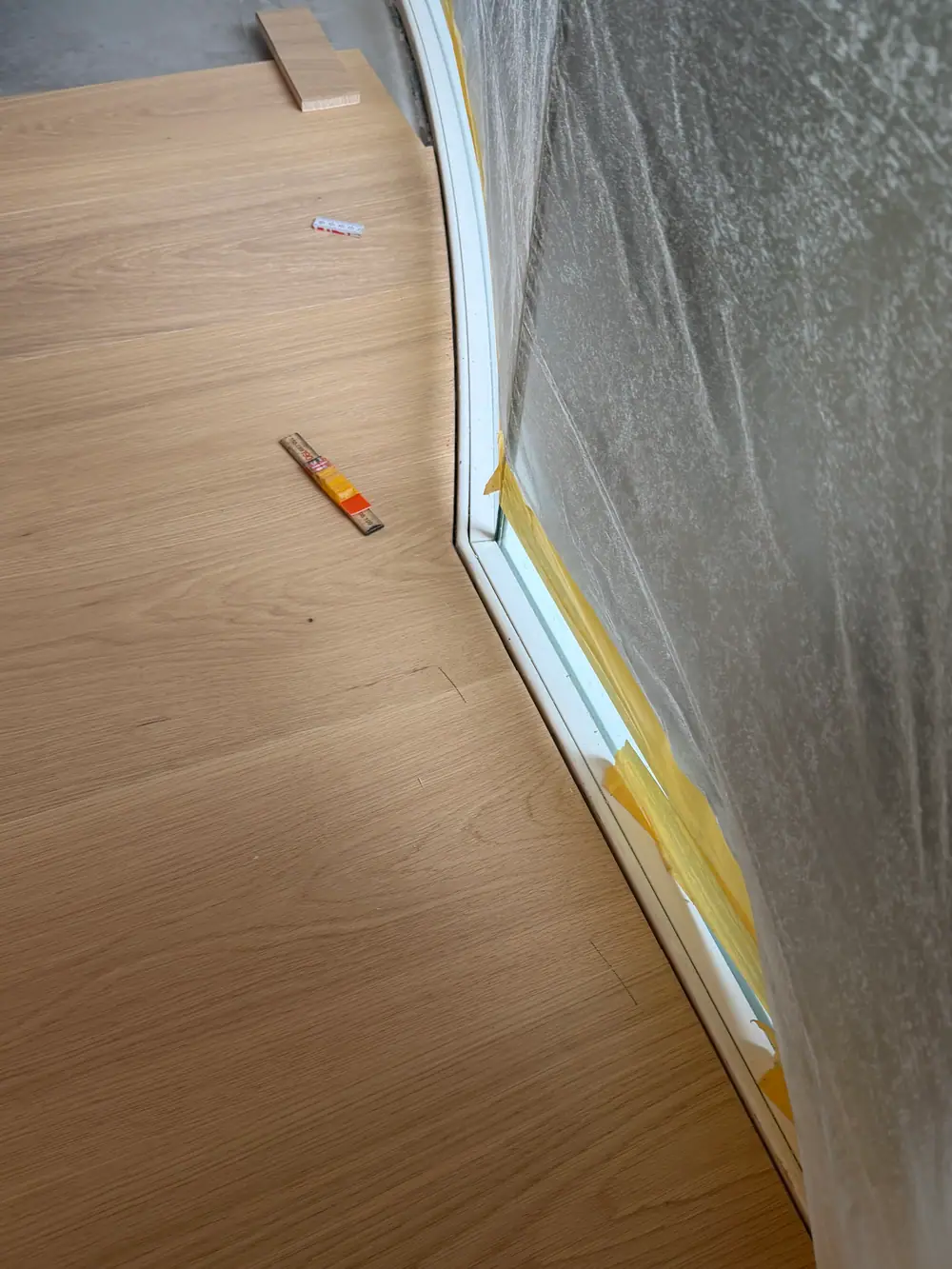 Reihe heller Holzdielen entlang einer grauen Wand während der Verlegung.