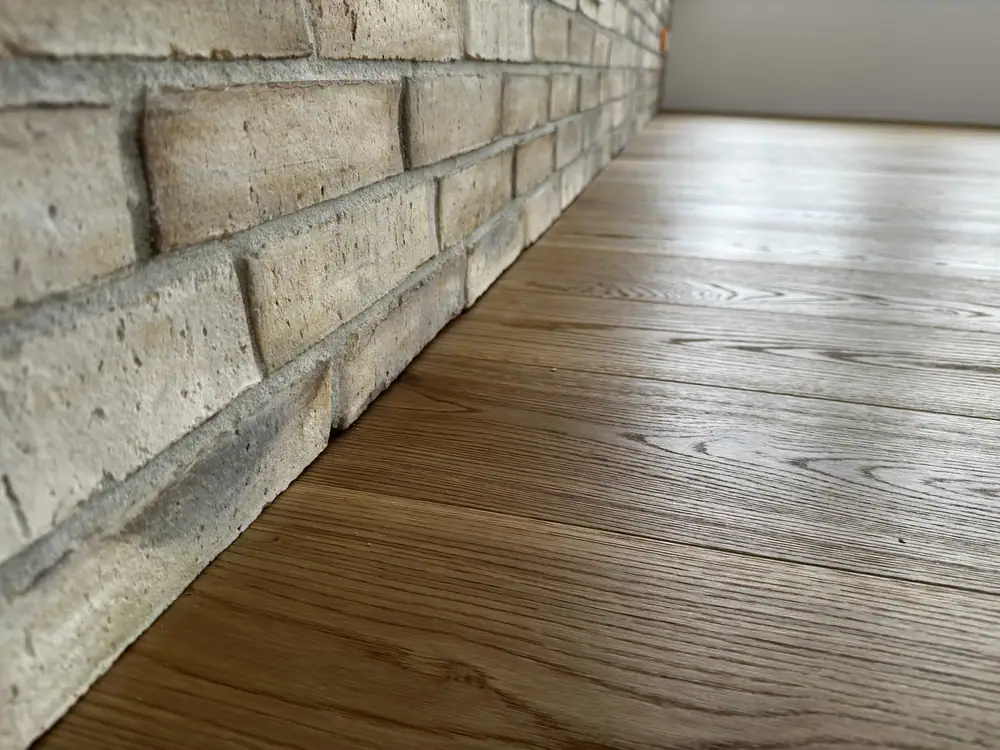 Bodennaher Blick entlang einer strukturierten Steinwand auf den passgenauen Anschluss des Holzbodens.