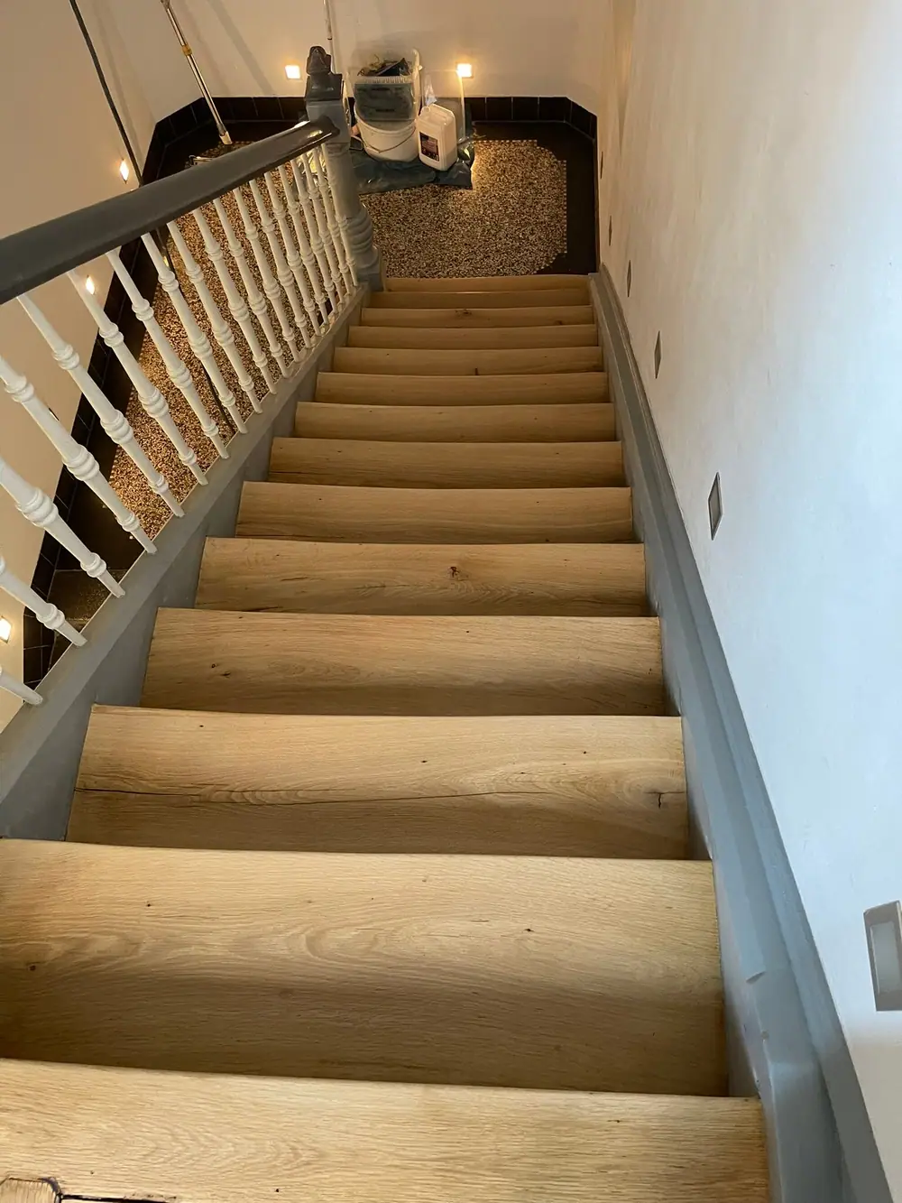 Blick von oben auf einen hellen geraden Treppenlauf mit weißem Geländer und grauen Wangen.