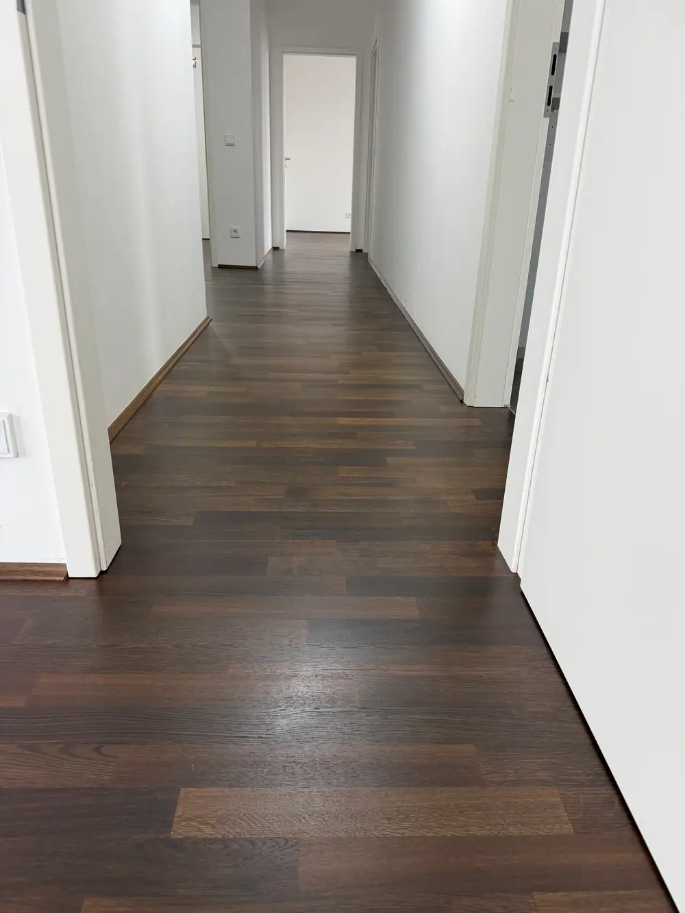 Dunkler Holzboden in einem Flur zwischen weißen Türrahmen.
