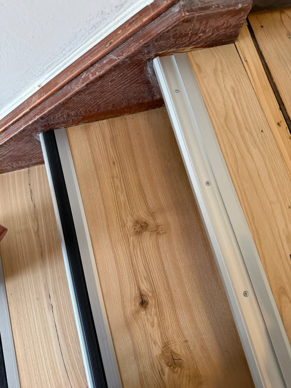 Nahaufnahme einer hellen Holztrittfläche mit silberfarbener Aluminium-Schutzkante und schwarzer geriffelter Gummieinlage.