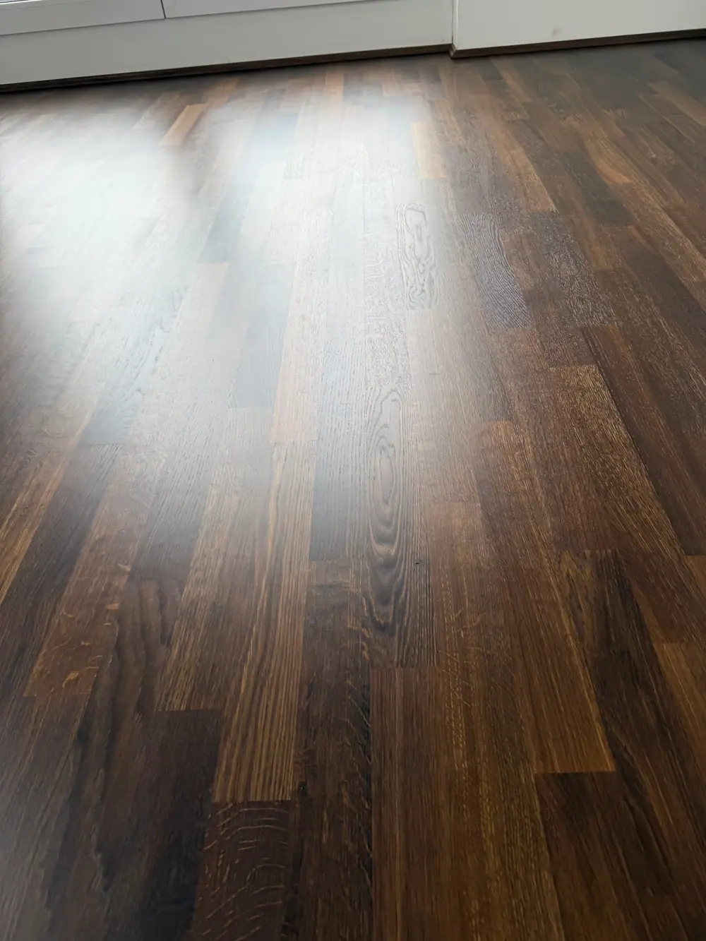 Nahaufnahme eines dunklen Holzbodens mit starker heller Lichtspiegelung und sichtbarer Maserung.