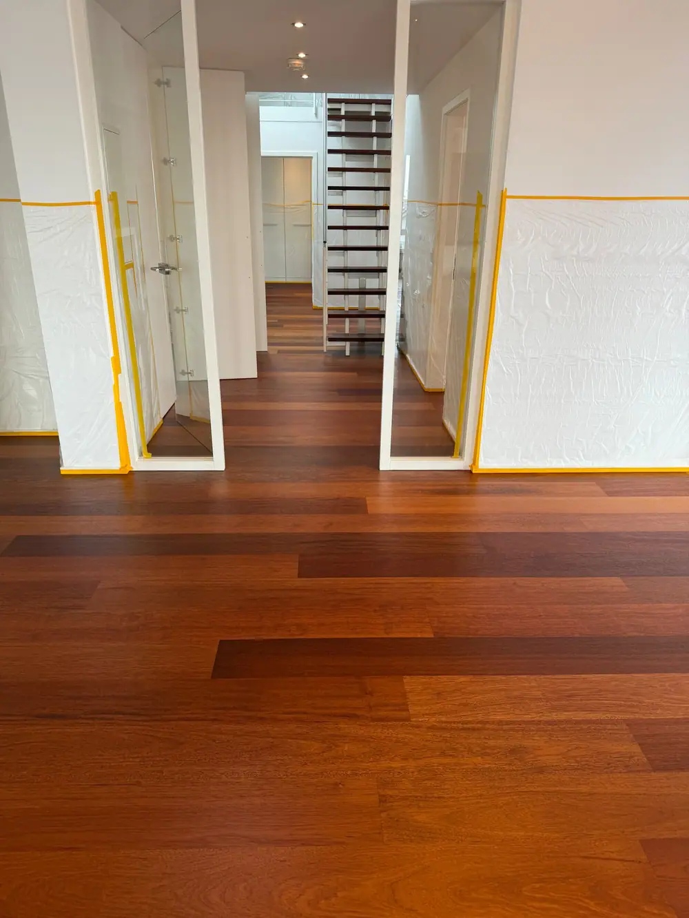 Dunkler Dielenboden im Durchgang mit Glastüren, abgedeckten Wänden und offener Treppe im Hintergrund.