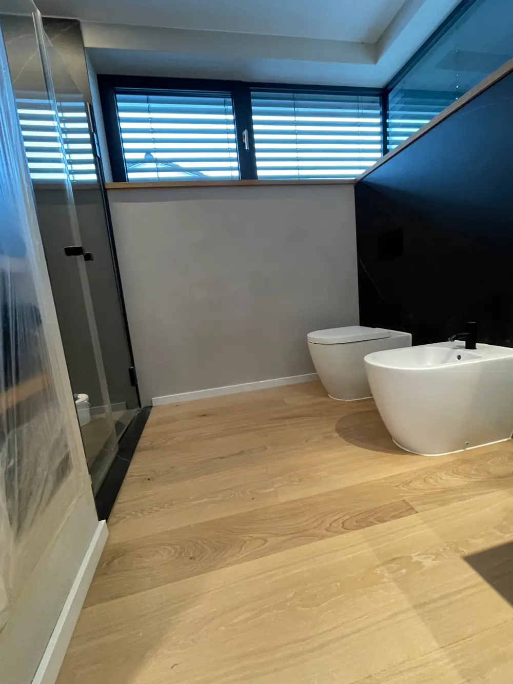 Heller Eichenboden in einem Bad mit weißem WC, Bidet und Duschglaswand.