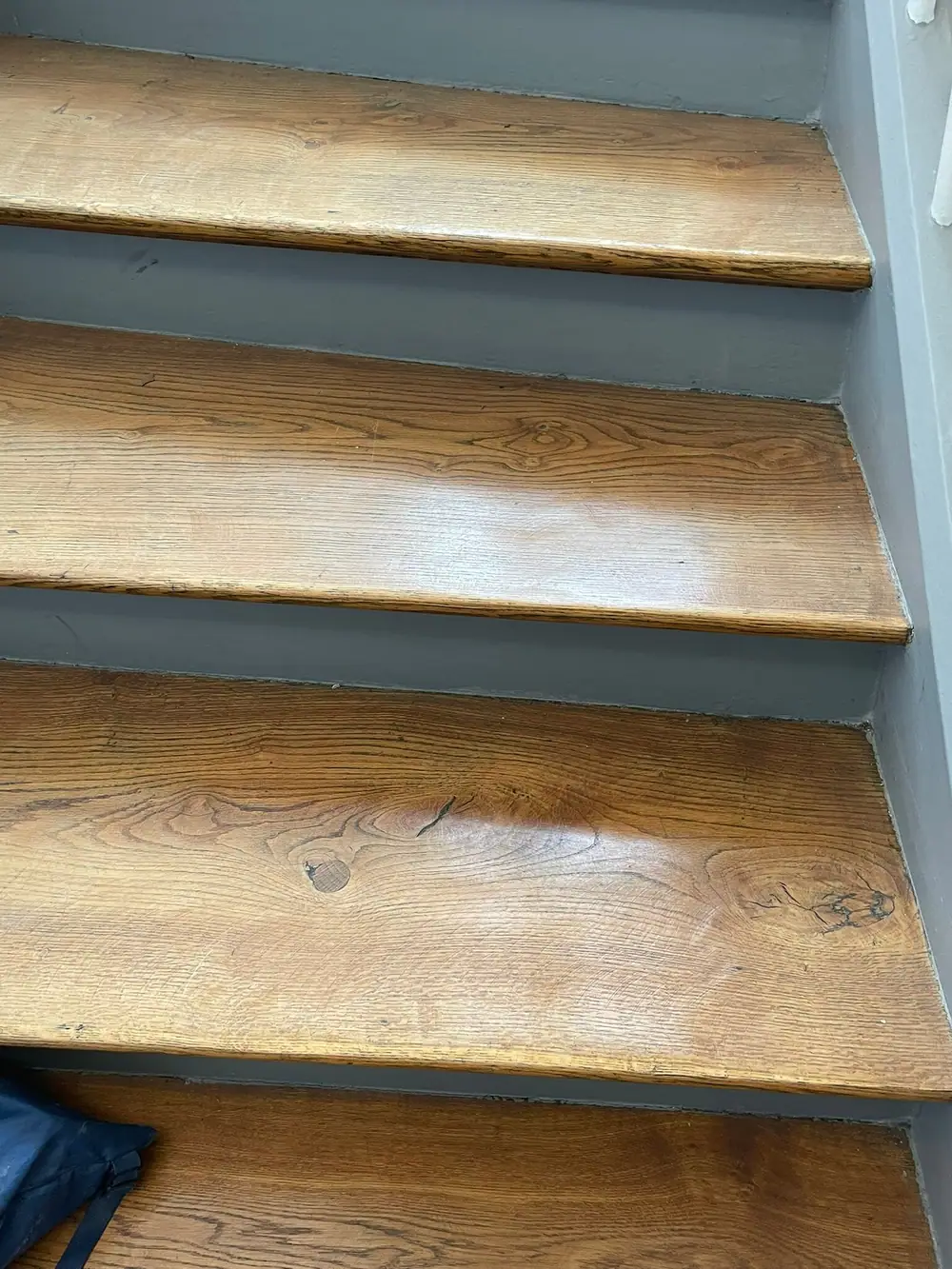 Nahaufnahme älterer Holzstufen mit dunklerer Oberfläche, sichtbaren Gebrauchsspuren und abgerundeten Vorderkanten.