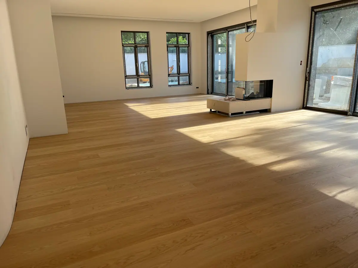 Heller Wohnraum mit breitem Dielenboden, hohen Fenstern und Sonnenlicht auf dem Boden.