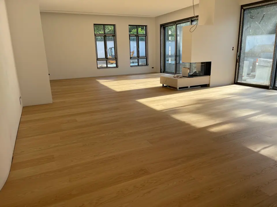 Heller Wohnraum mit breitem Dielenboden, hohen Fenstern und Sonnenlicht auf dem Boden.