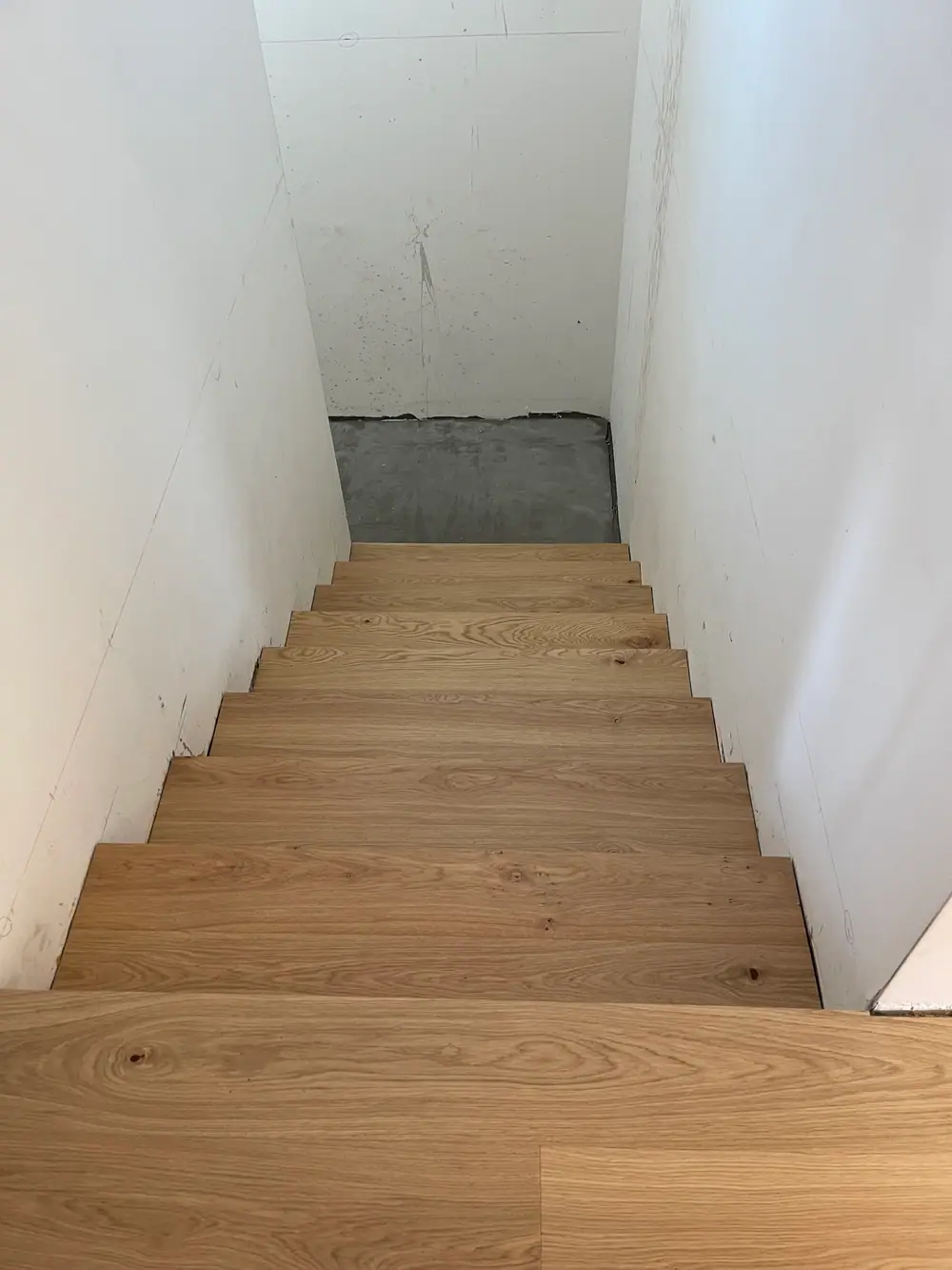 Unfertiger Treppenbereich mit grauem Betonabsatz und weißen, markierten Wänden.