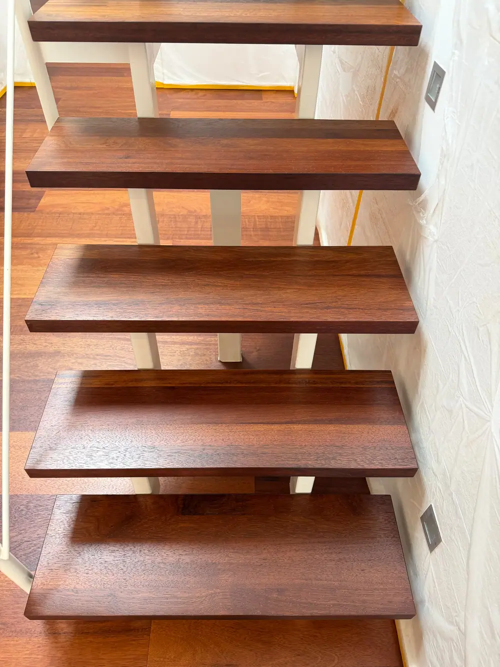 Blick von oben auf dunkle Holztrittstufen einer offenen Treppe mit weißem Geländer.