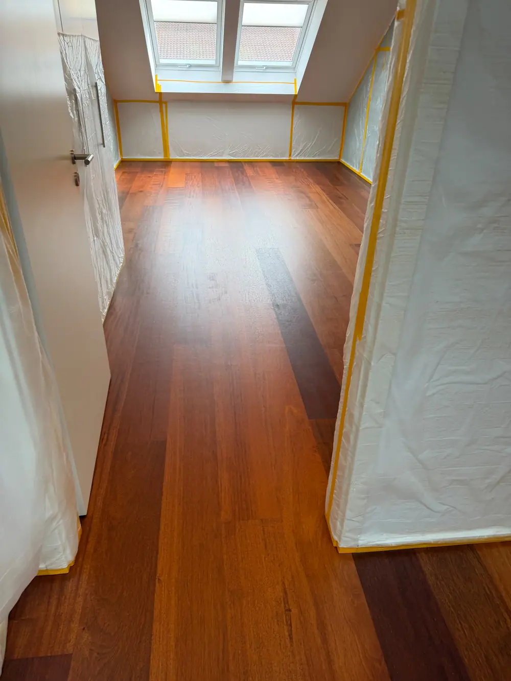 Kleiner Raum mit dunklem Landhausdielenparkett, zwei Dachfenstern und abgedeckten Wandflächen.