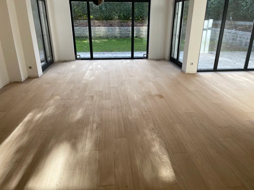 Großer Raum mit hellen Holzdielen, schwarzen Fensterrahmen und Blick in den Garten.