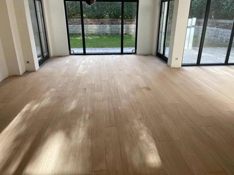 Großer Raum mit hellen Holzdielen, schwarzen Fensterrahmen und Blick in den Garten.
