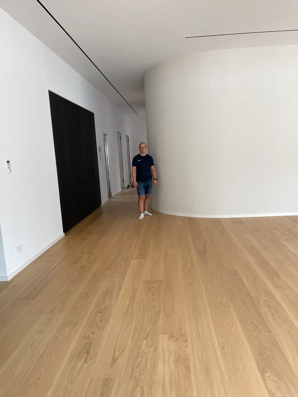 Heller Innenraum mit Holzdielenboden, geschwungener weißer Wand und dunkler Türfläche.