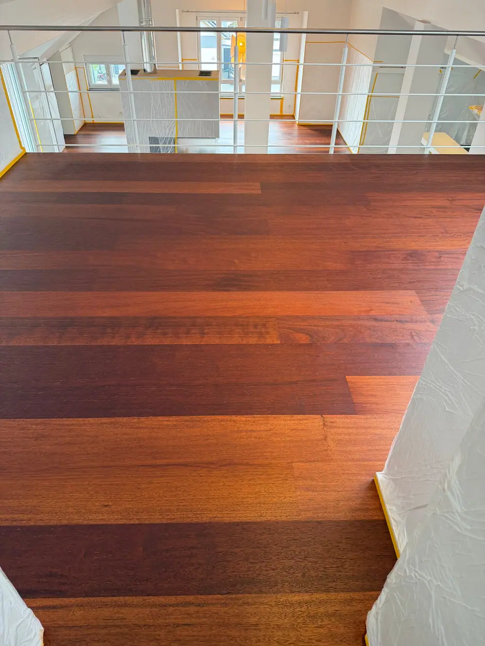Dunkles Landhausdielenparkett auf der Galerie vor weißem Geländer mit Blick in den darunterliegenden Wohnraum.