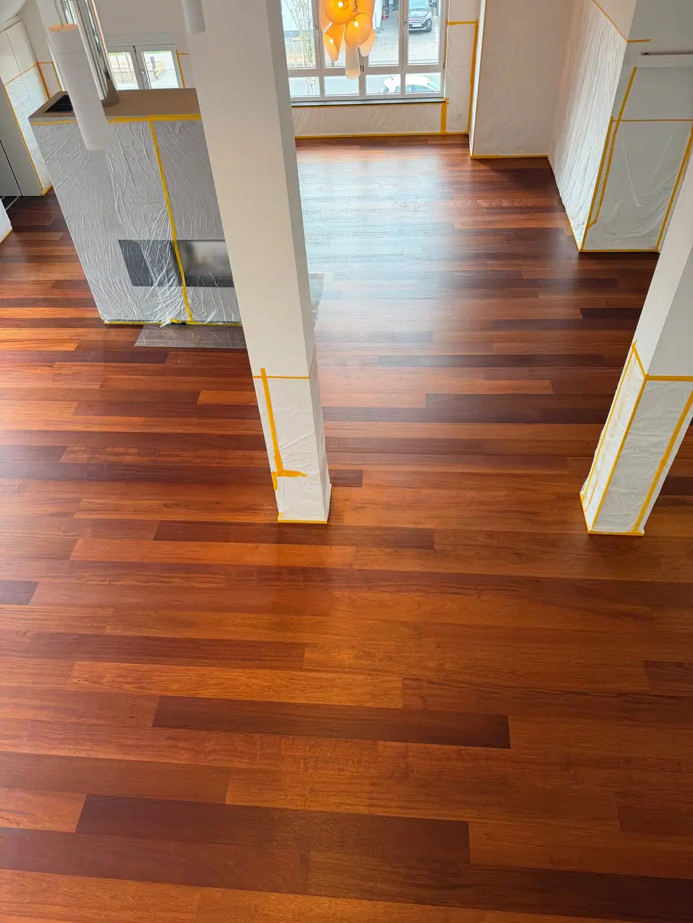Weitläufiger offener Wohnbereich mit dunklem Landhausdielenparkett, abgedeckten Stützen und großen Fenstern.