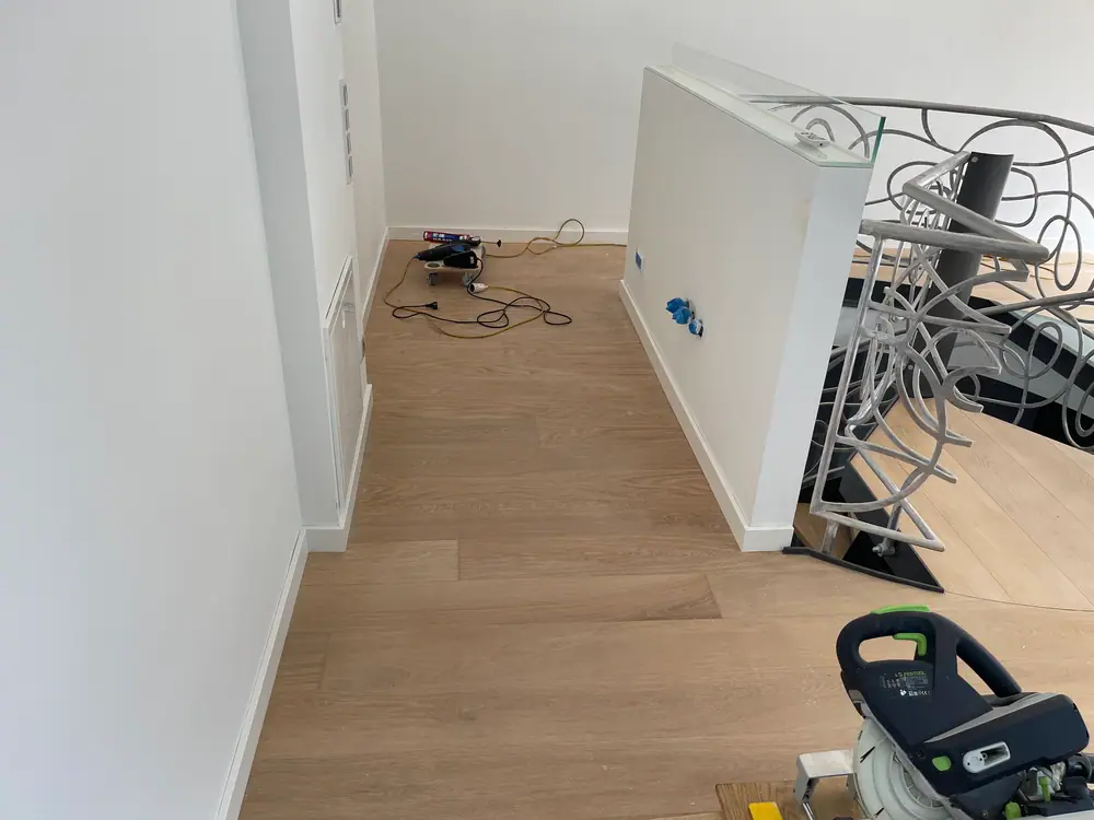 Helle Dielenfläche am Treppenpodest mit weißer Brüstung, Metallgeländer und Arbeitsgeräten.